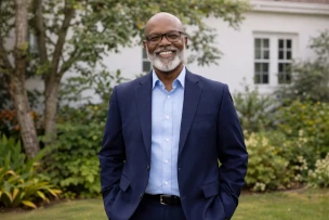 Foto de um senhor preto, calvo, com barba branca curta, vestindo uma roupa social azul